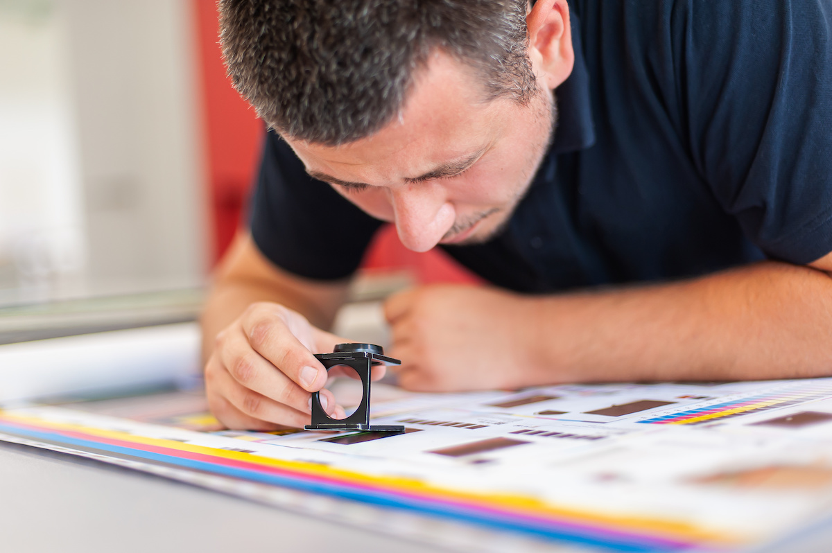 Young man in the process of printing used color scales and loupe and management color correction. Spectrophotometer, print measuring.